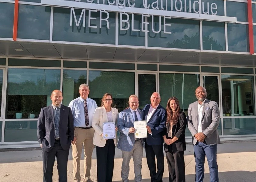 Des dignitaires et des membres de l’administration scolaire réunis devant le Collège catholique Mer Bleue pour célébrer le 10e anniversaire de l’école. Deux personnes tiennent des certificats commémoratifs.