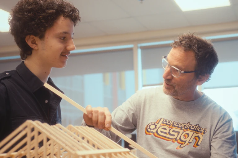 Un enseignant avec ses lunettes de protection, qui construit avec un élève une maquette de maison en bois
